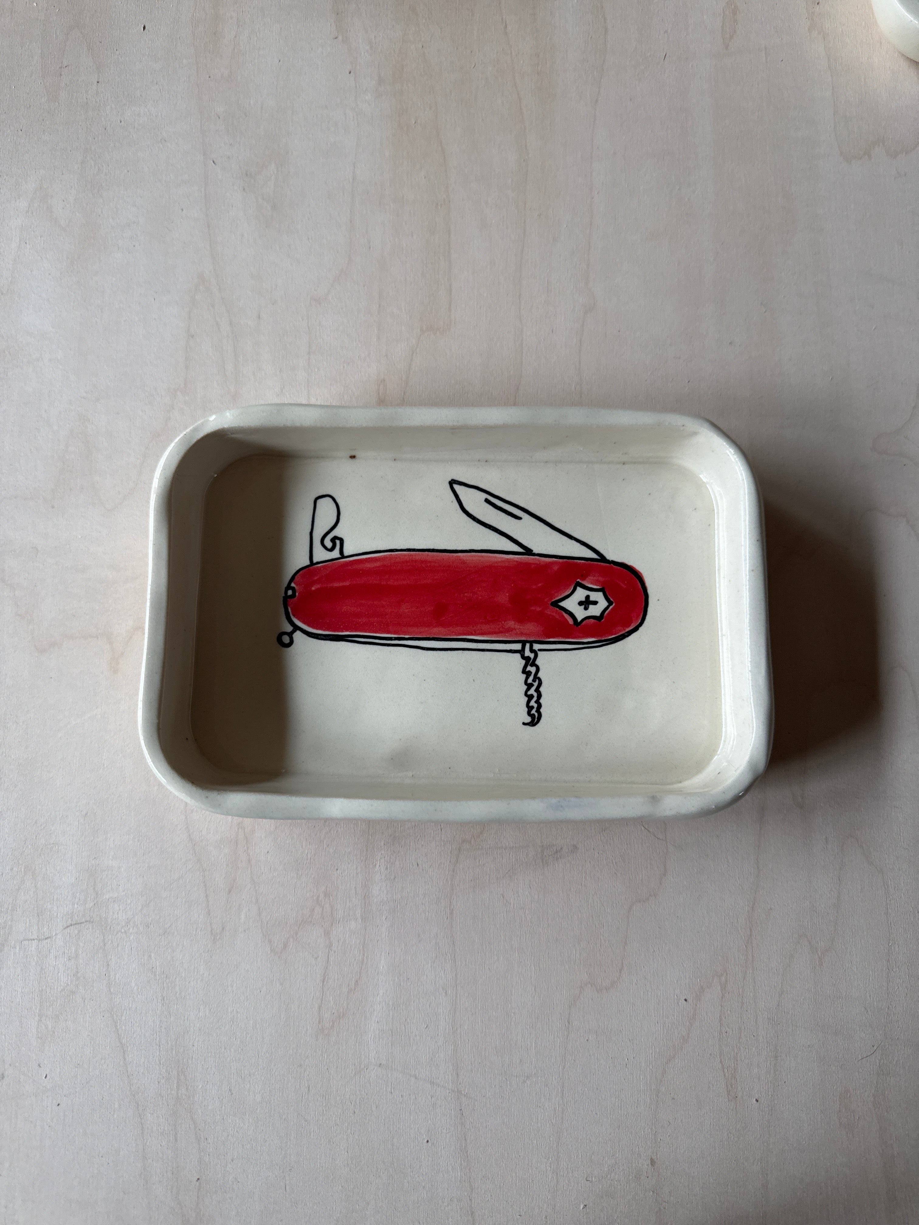 White rectangular dish with a red Swiss Army knife illustration on a light wooden surface